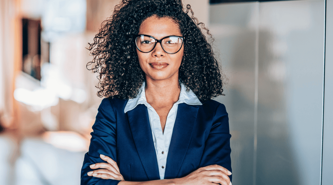 Professional-looking woman in a suit and glasses, standing with her arms crossed.